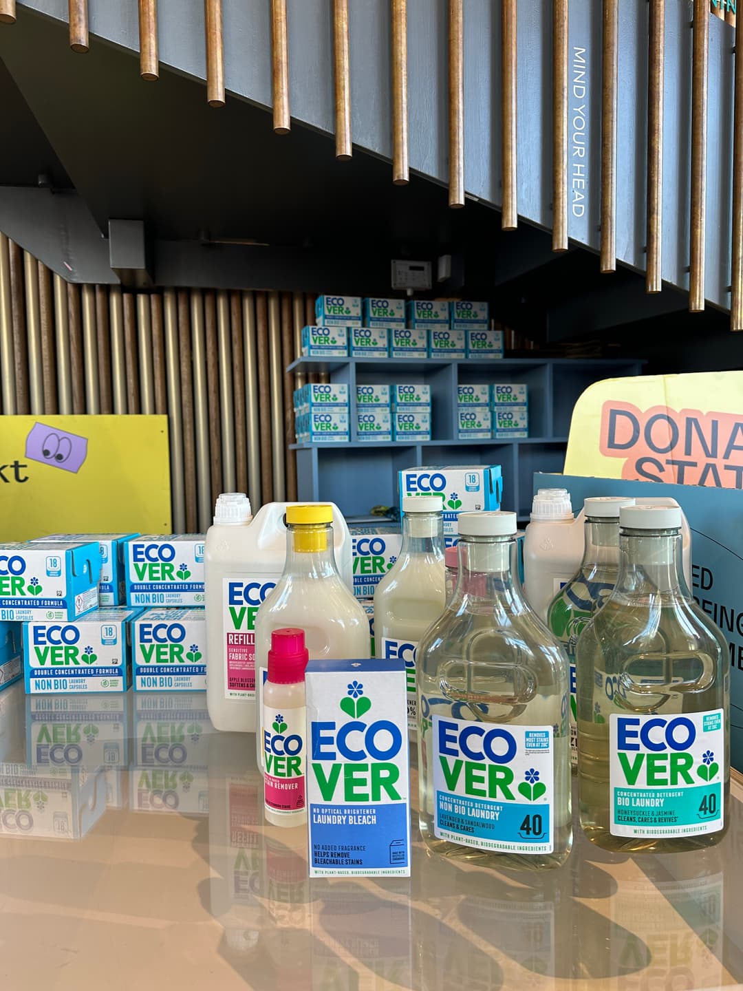 Bottles of Ecover cleaning products displayed on a table, including non-bio laundry detergent and refill bottles, with boxes in the background.