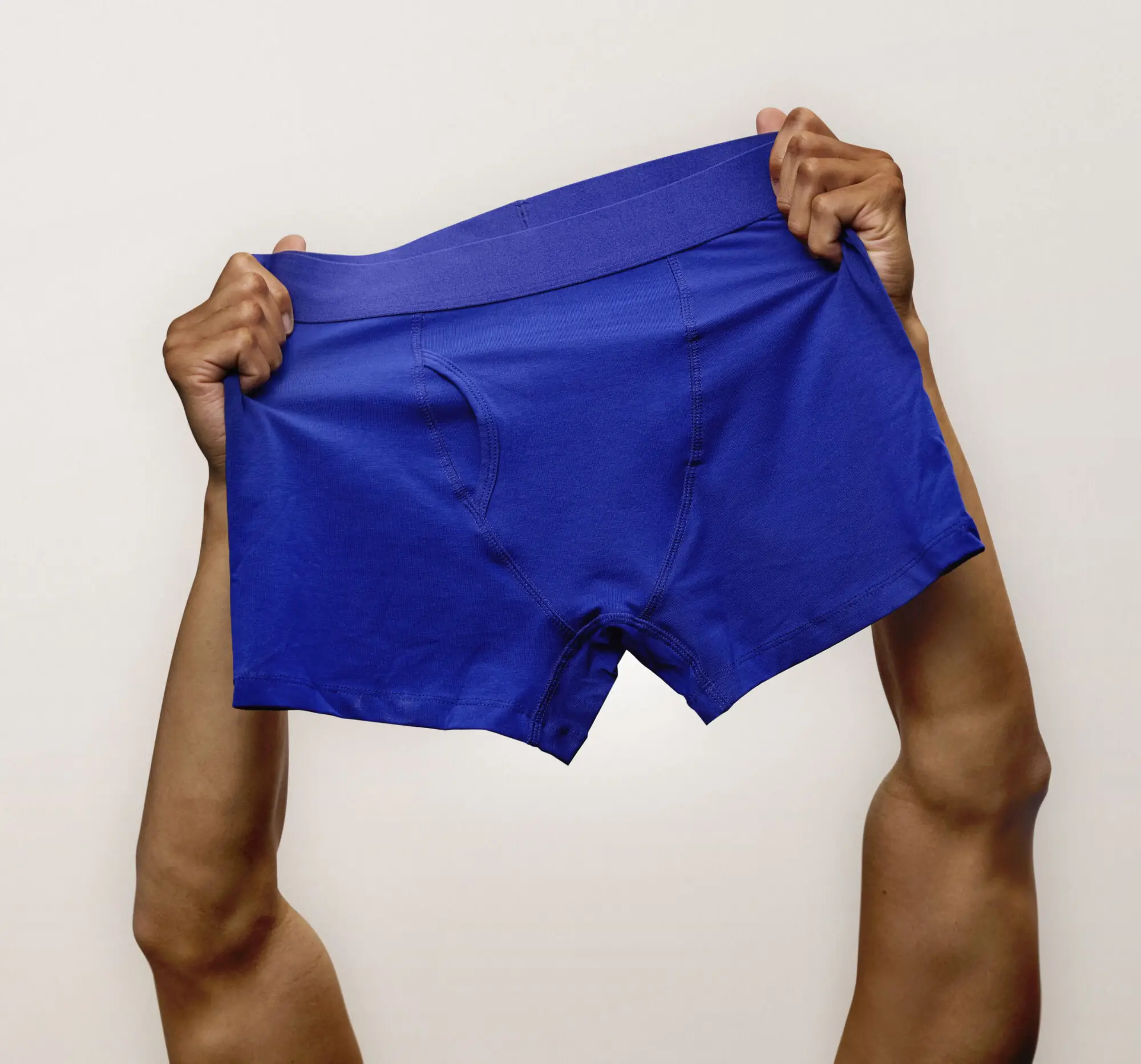 Person holding up a pair of blue boxer briefs against a plain background.